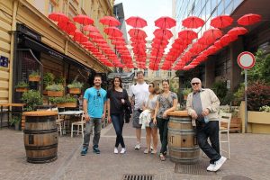 Group of tourists on Belgrade private city tour are posing in pedestrian area with red umbrellas.
