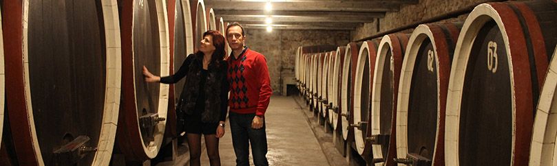 Married couple is standing between wine barrels of Royal wine cellar in Oplenac in Serbia