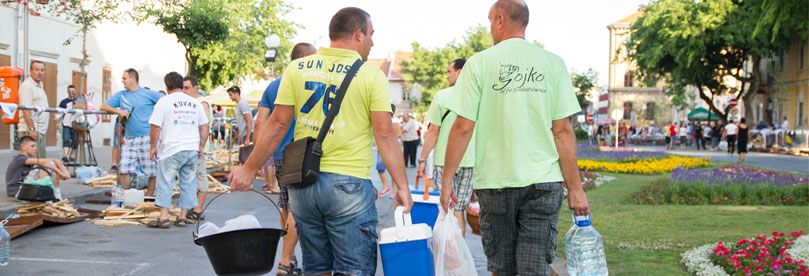 Two guys in yellow and green shirt are taking fishpot and other ingredients for fish stew in Sombor